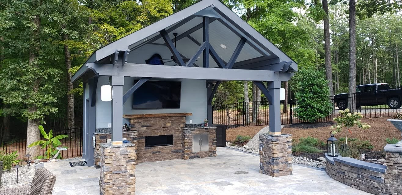 Covered gazebo-style patio with stone fireplace, TV, and outdoor kitchen